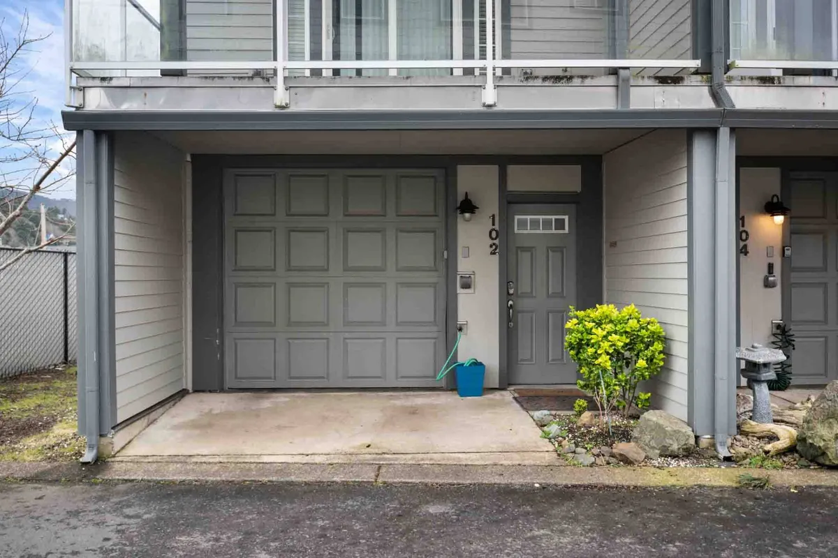 A view of the townhouse's front entrance with a garage door, welcoming front door, and a planter with greenery. The scene radiates a sense of arrival and neighborhood warmth, hinting at the proximity to both the beach and local attractions.