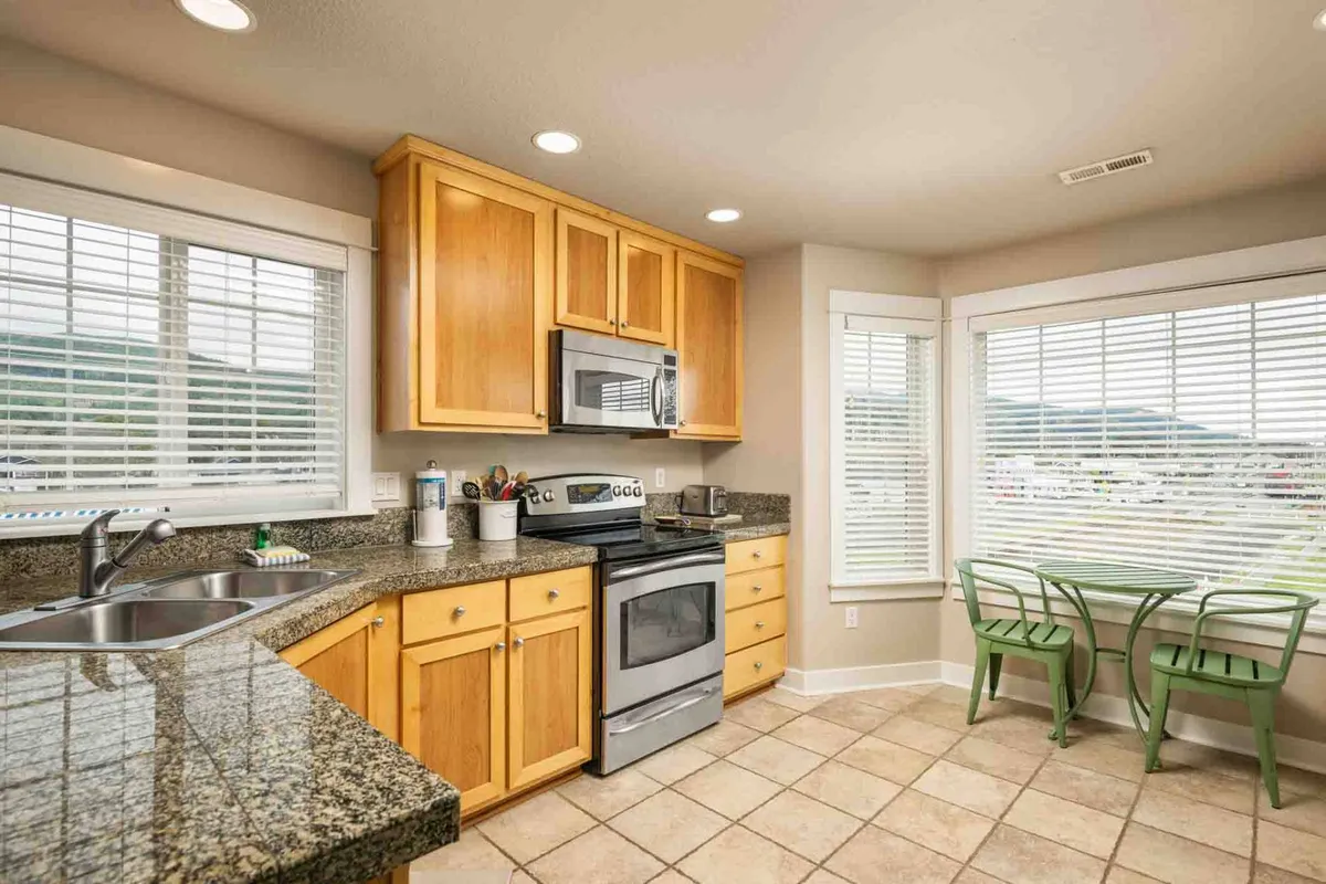 This image features a bright kitchen and dining nook with granite countertops, stainless steel appliances, and inviting green chairs positioned around a cozy breakfast table. The sunlight pours through the windows, highlighting the welcoming atmosphere. The layout encourages casual gatherings for coffee or meals before heading out to explore.
