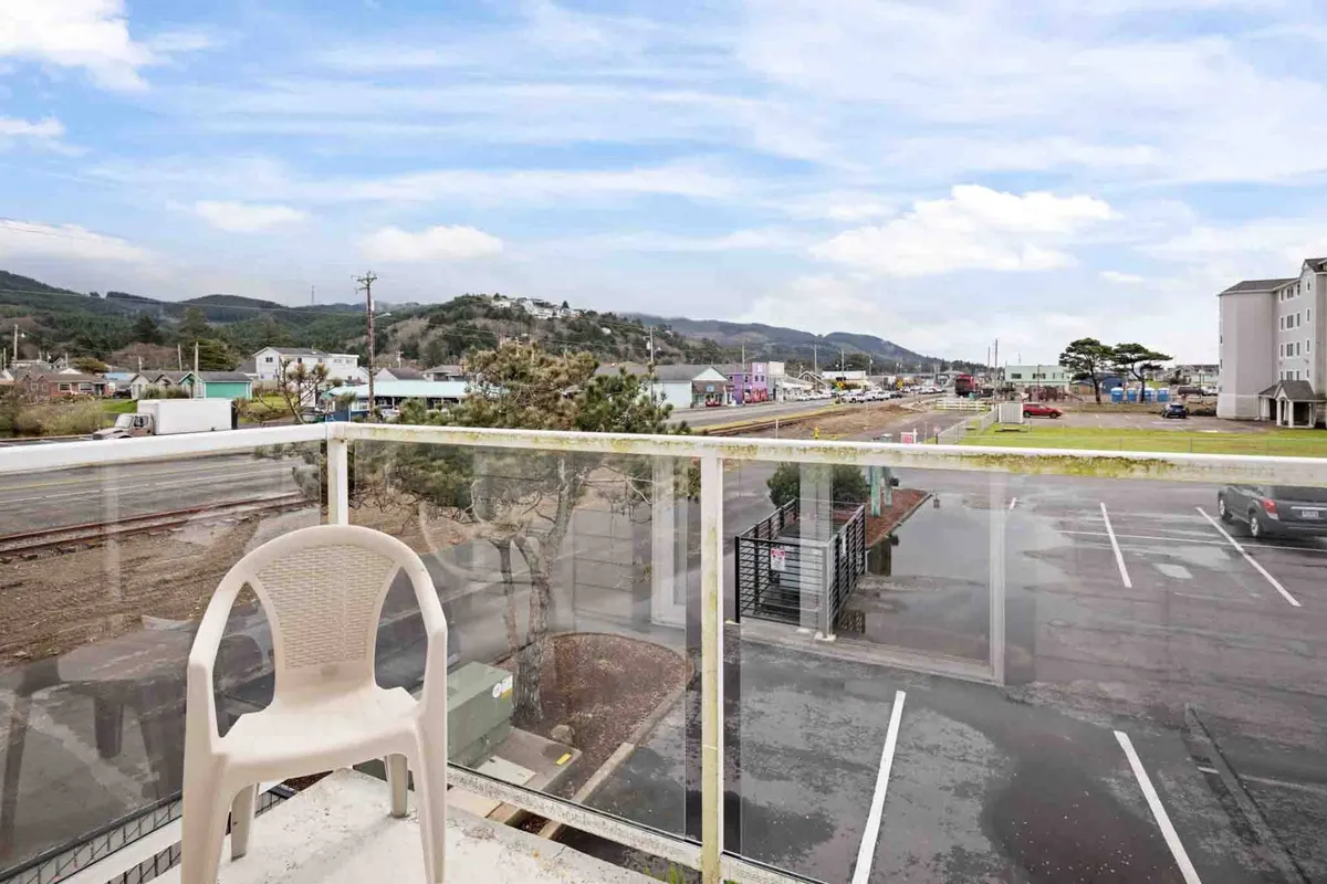 A serene balcony with a comfortable chair overlooks distant mountains and nearby buildings. The open space is bathed in natural light, offering the perfect spot to enjoy morning coffee, read a book, or simply watch the sunset as gentle breezes flow through. The setting suggests a private outdoor retreat with a direct connection to the natural surroundings.