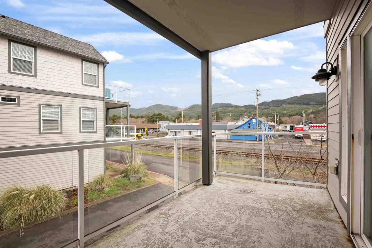 An inviting balcony, enclosed by a sturdy railing, frames picturesque mountain views and adjacent buildings. The covered aspect of the space provides comfort and usability throughout the seasons, making it ideal for outdoor dining, stargazing, or small gatherings regardless of weather.