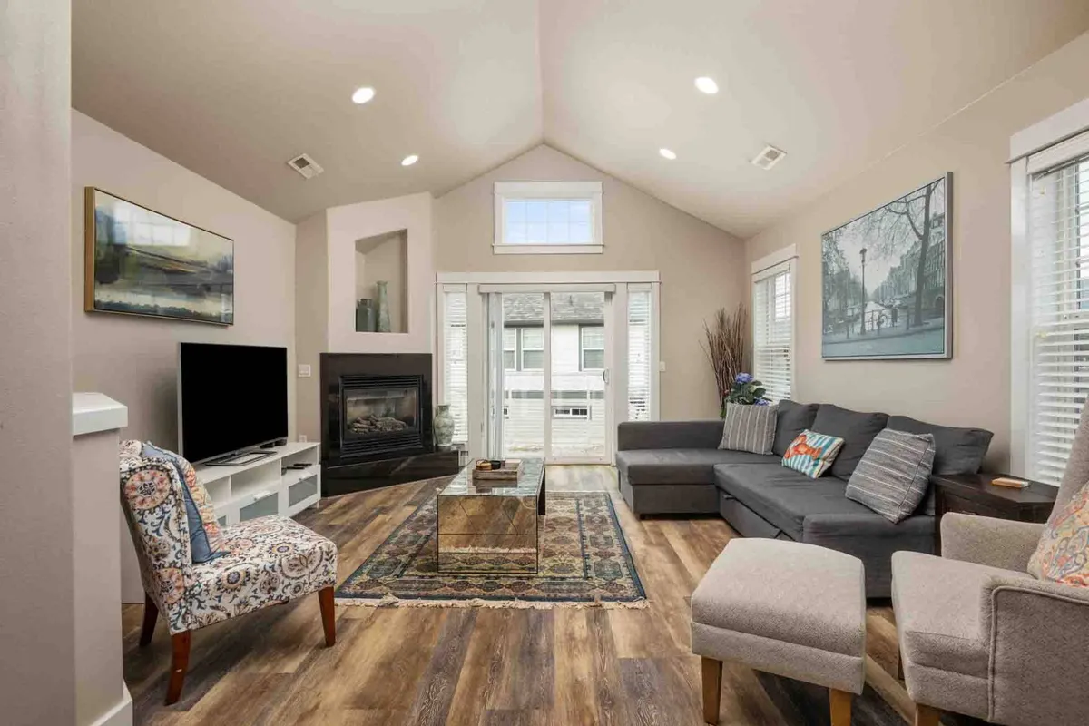 A spacious, sun-filled living room featuring a soft, inviting sofa, a modern fireplace, a central coffee table, decorative artwork, and sliding doors that flood the space with natural light. The area radiates warmth and openness, ideal for gathering and relaxing.
